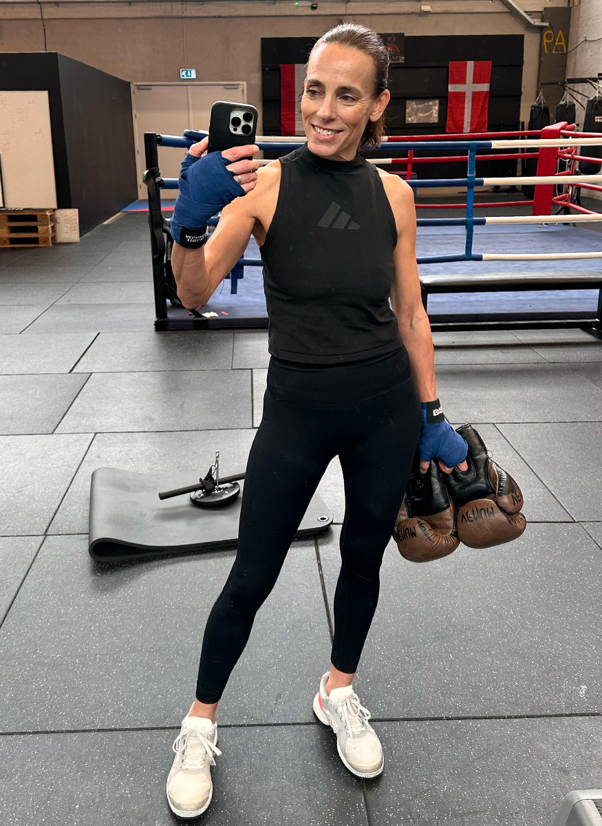 Coach Camilla in gym wear and hand wraps, holding boxing gloves for a selfie.